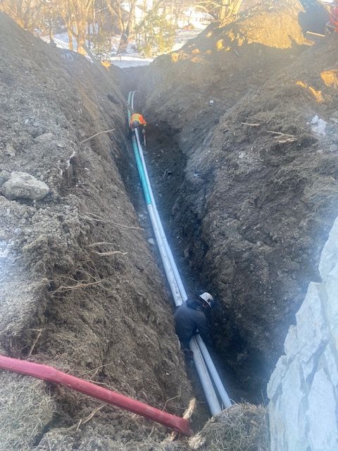 Deux ouvriers du bâtiment installent des canalisations dans une tranchée de terre profonde et étroite.