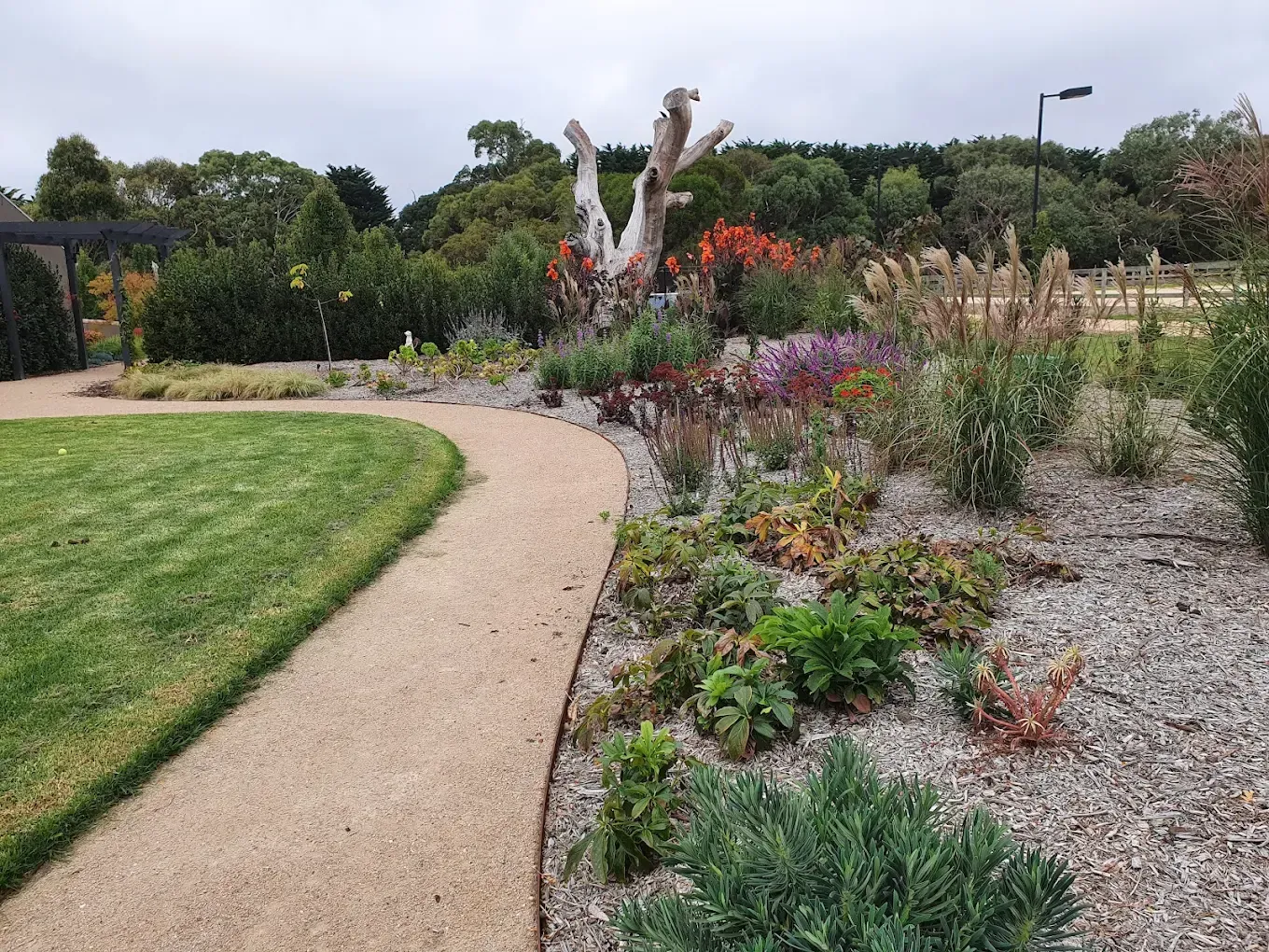Stone path winds through garden beds with colorful flowers and ornamental grasses.
