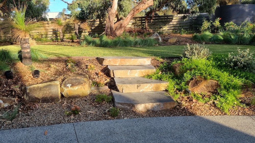 Stone path winds through garden beds with colorful flowers and ornamental grasses.