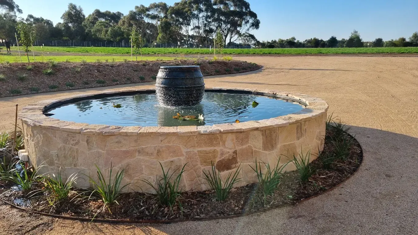 Fountain in stone basin with stone steps and gravel path in a garden.