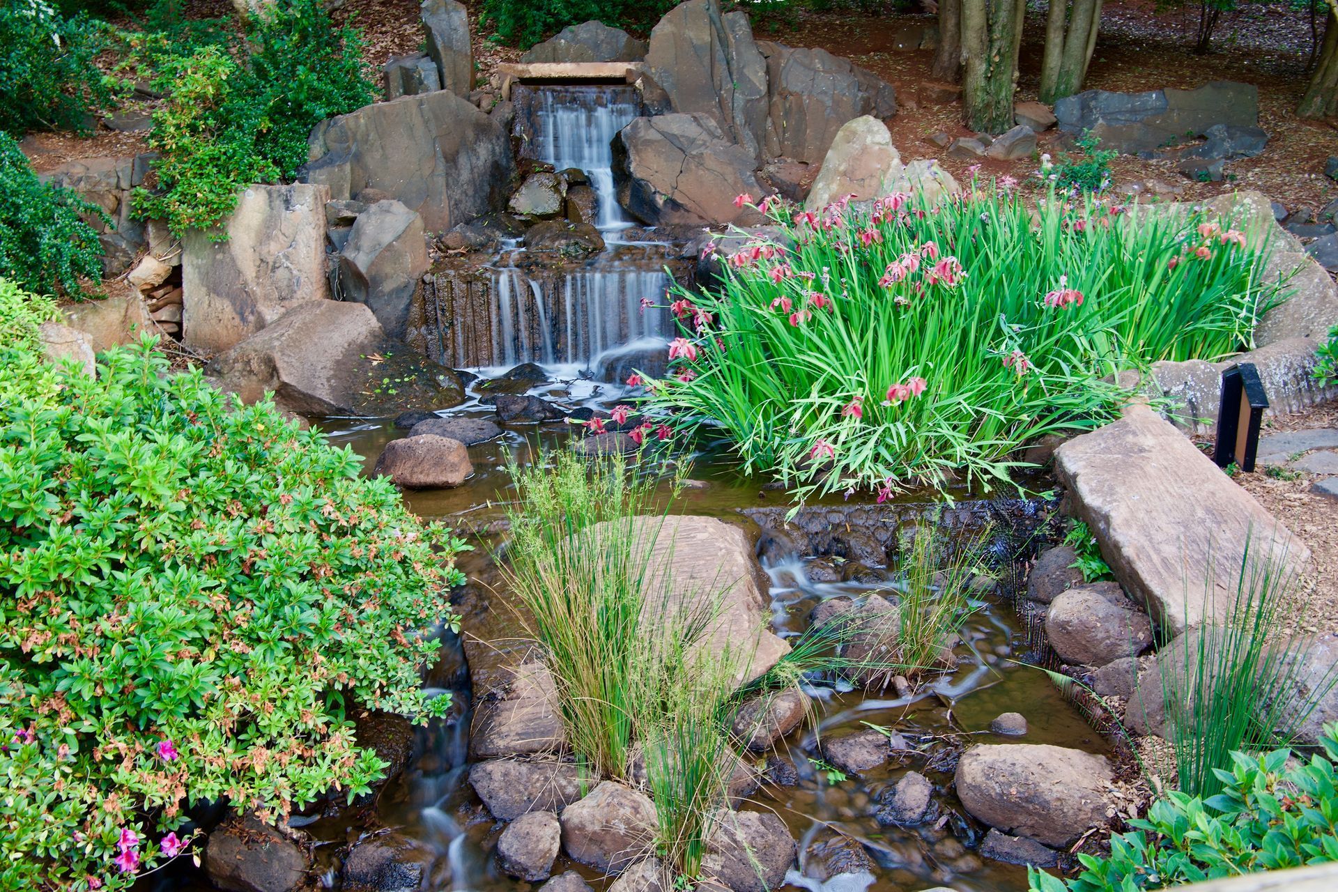 Stone path winds through garden beds with colorful flowers and ornamental grasses.