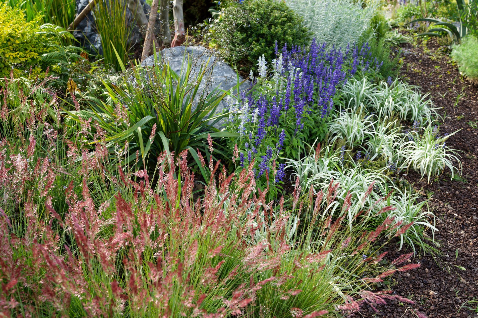 Stone path winds through garden beds with colorful flowers and ornamental grasses.