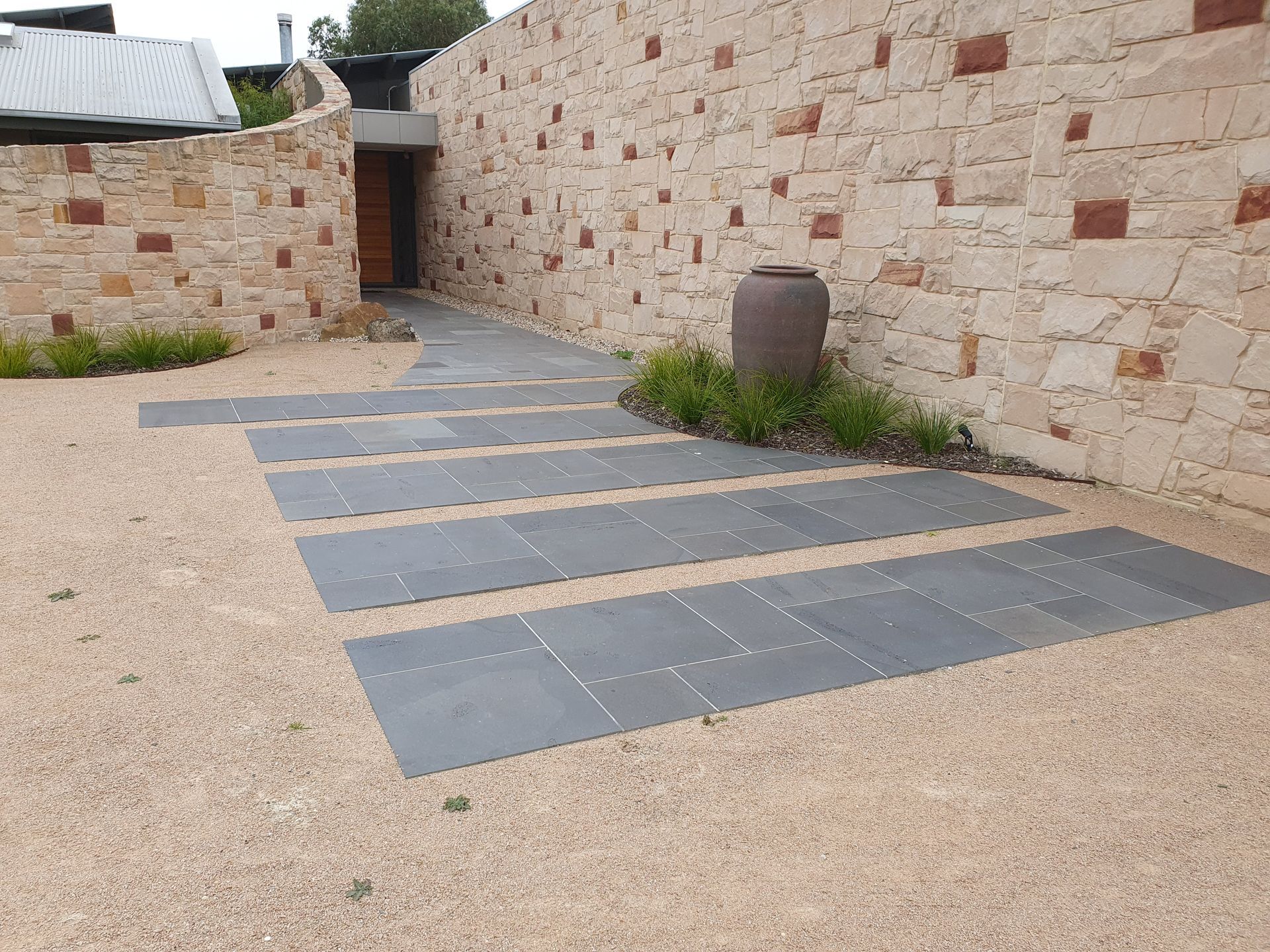 Stone walkway with rectangular pavers, gravel, and stone walls leading to a wooden door.
