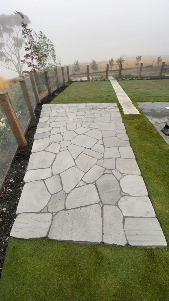 Stone walkway surrounded by artificial turf and a wooden fence. Overcast sky in the background.