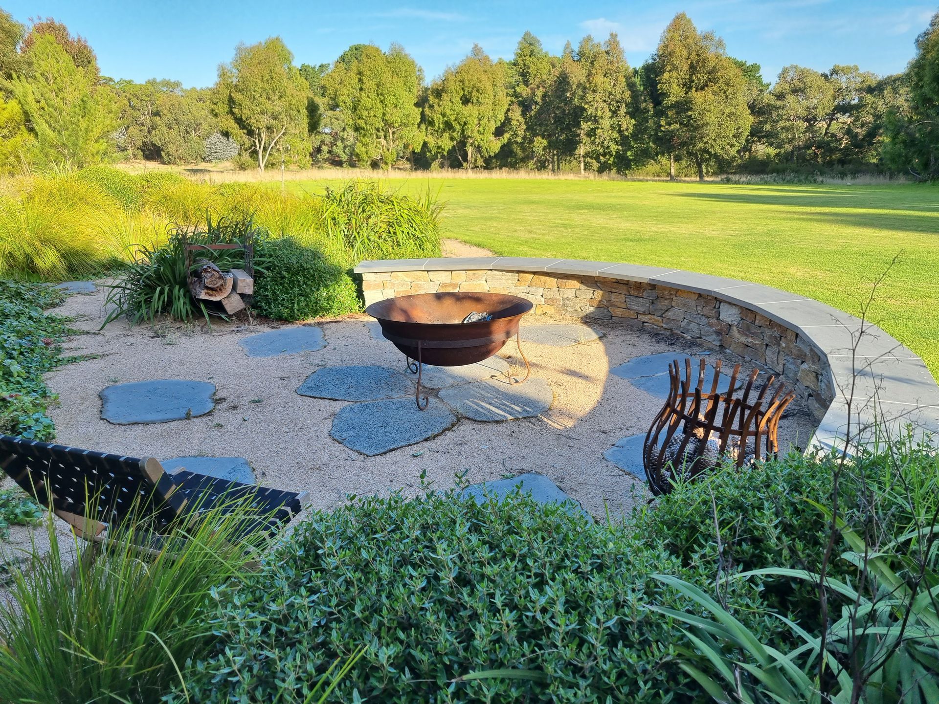 Fire pit area with stone wall, gravel, and trees in background.