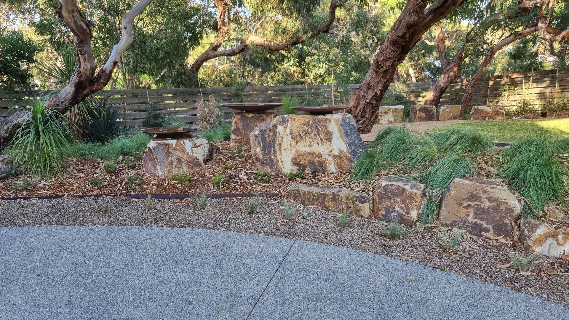 Lush green grasses and plants surround a small pond with rocks and a gravel pathway.
