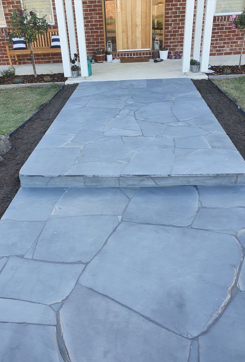 Flagstone walkway leading to a front door with porch columns. Steps lead to entrance.