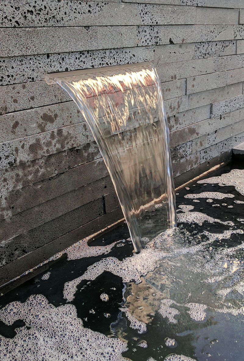 Waterfall flowing from a ledge into a pool; gray stone wall in the background.