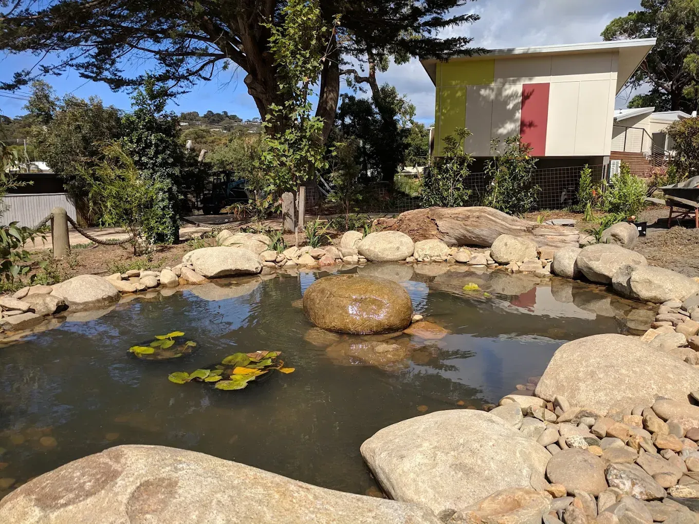 A small pond surrounded by rocks with a water fountain in a garden setting.