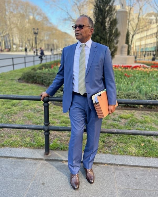 A man in a suit and tie is standing next to a fence holding a book.