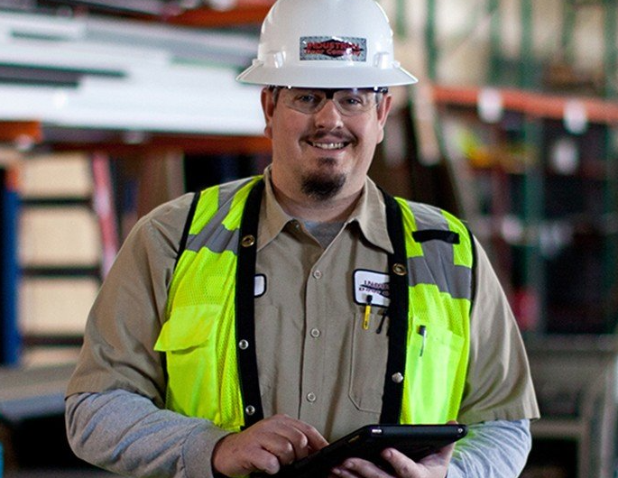 a man wearing a hard hat and safety vest is holding a tablet .