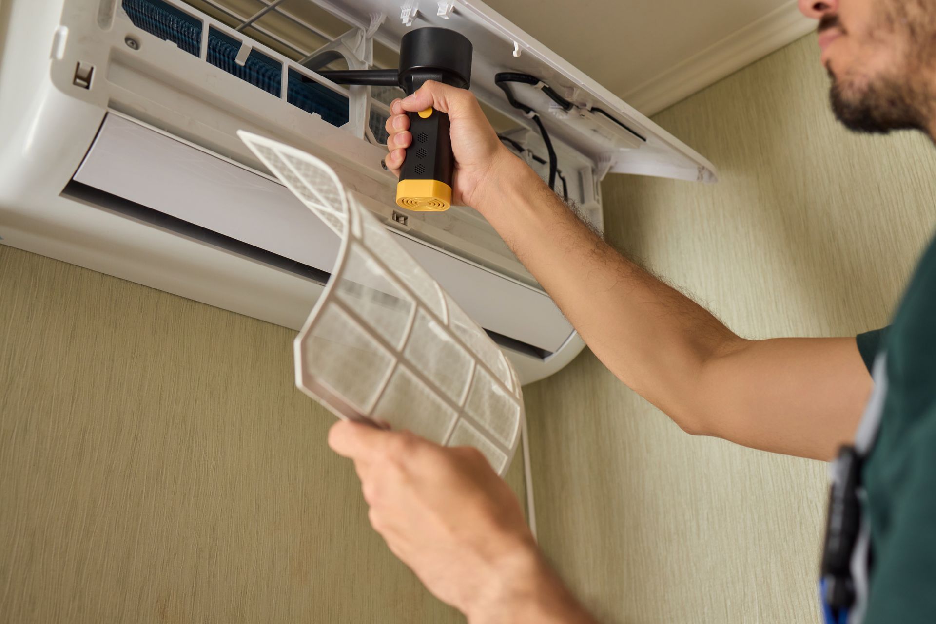 Person inspecting an air conditioner, holding a filter and flashlight indoors.