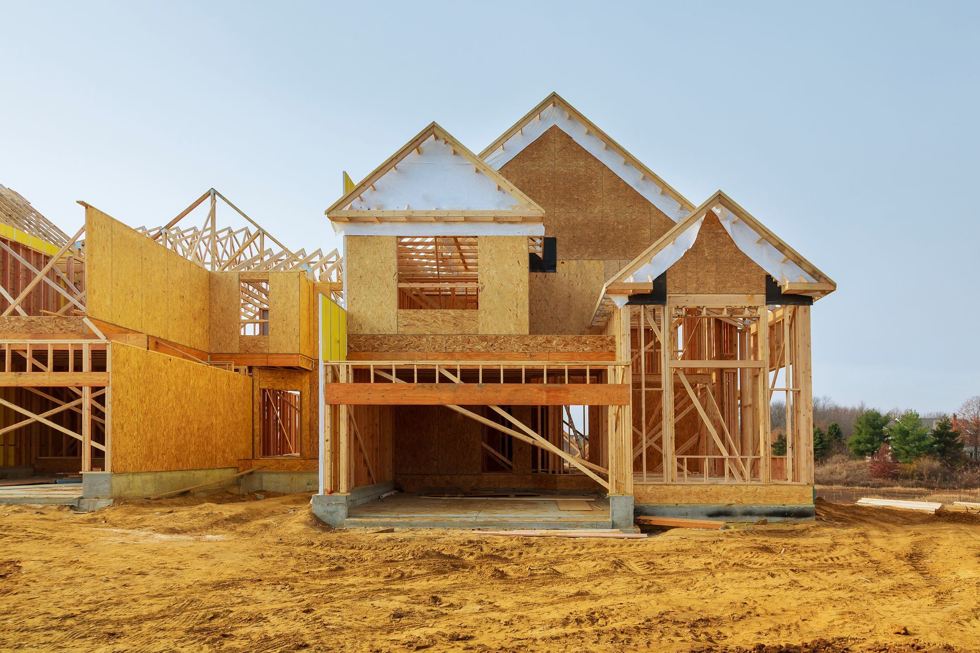 Wooden house under construction; exposed framing, unfinished exterior, and dirt lot.