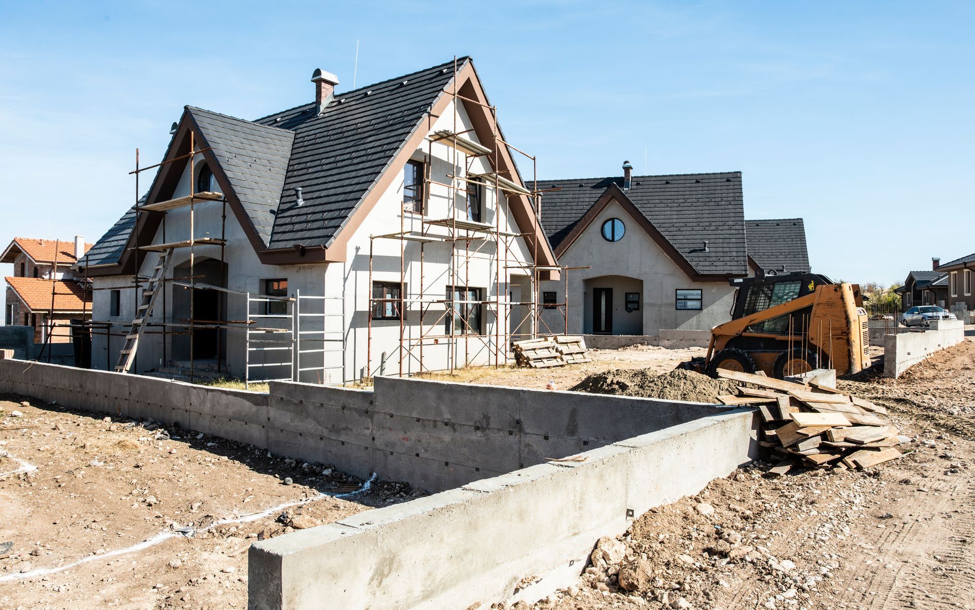 Houses under construction with scaffolding and a cement barrier.