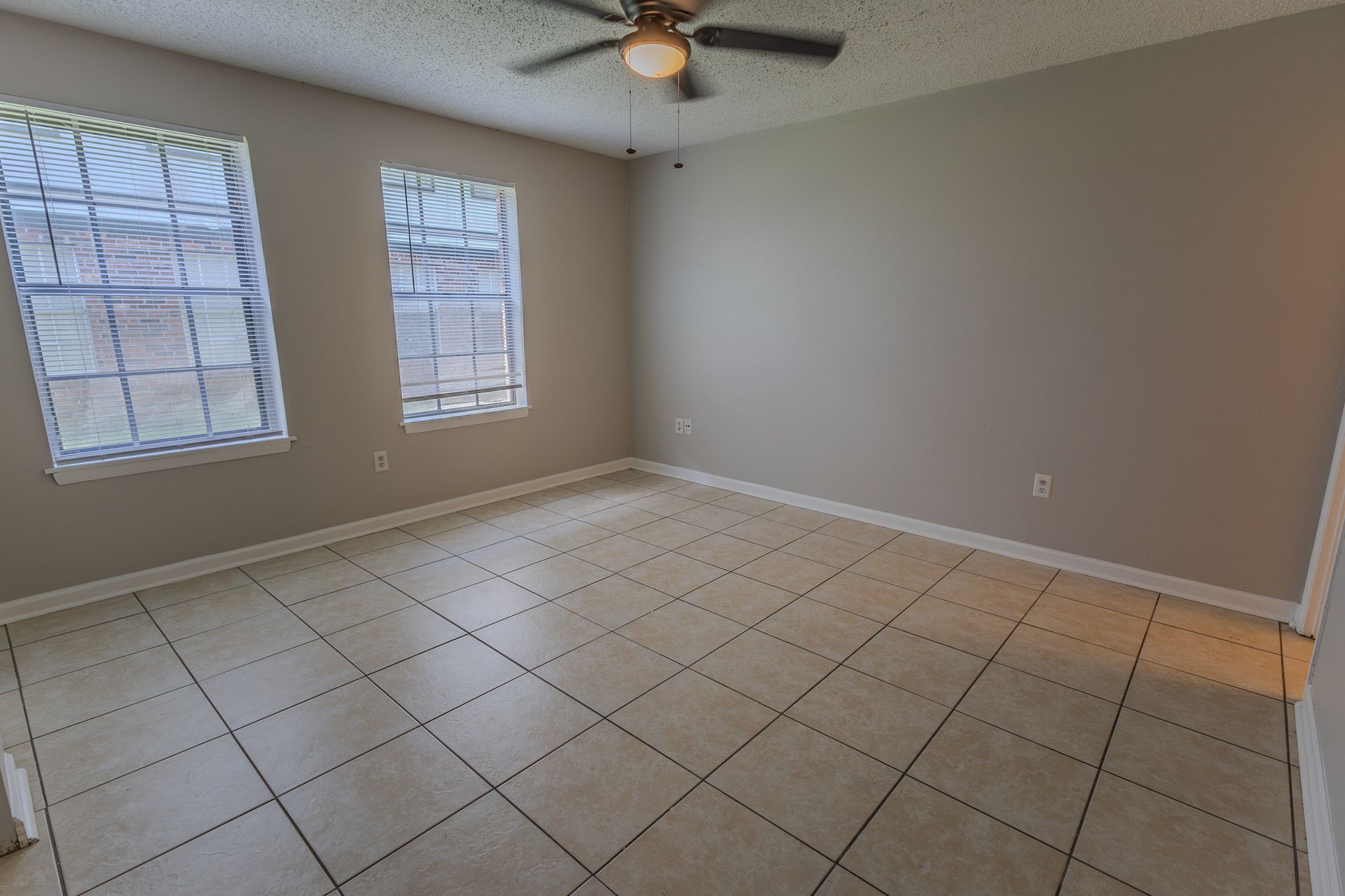 Empty room with tile floor, two windows, gray walls, and a ceiling fan.