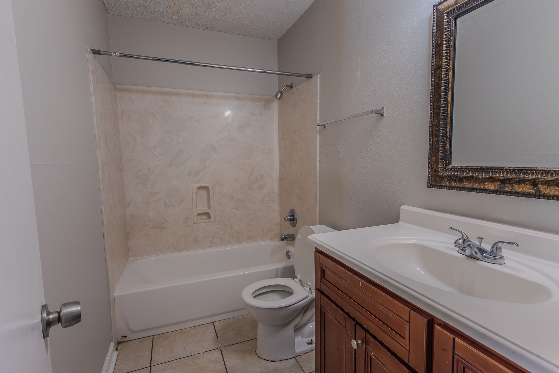 Bathroom with tub, toilet, vanity, and large mirror. Neutral walls, brown cabinets, and beige shower surround.