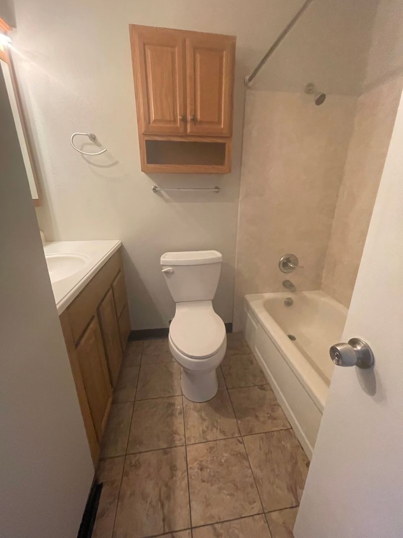 Bathroom with toilet, tub, vanity with sink, and cabinet above toilet.