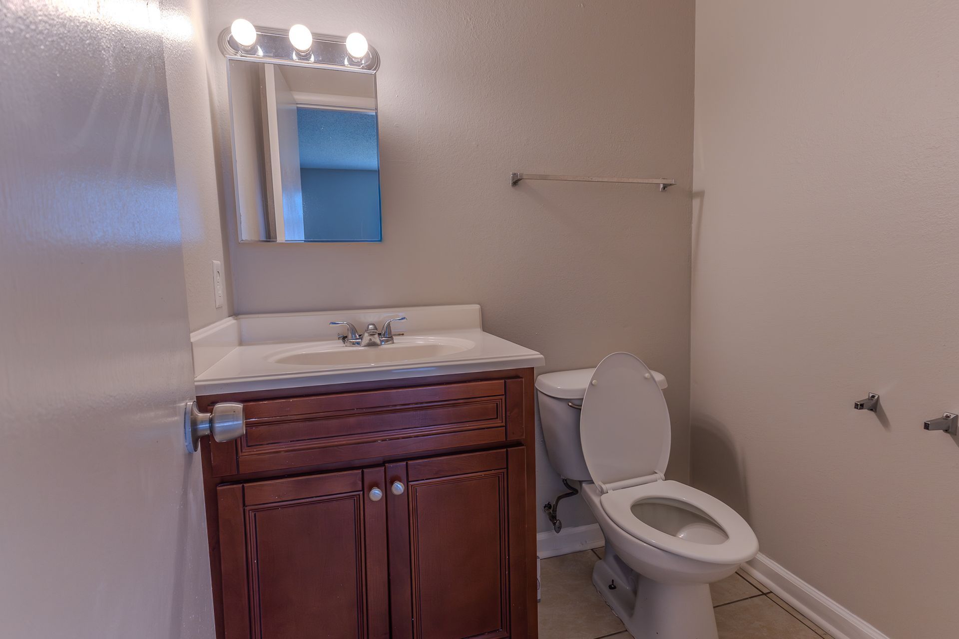 Bathroom with vanity, toilet, and towel rack; tan walls, brown cabinet, white sink, and toilet.