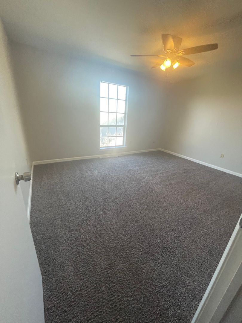 Empty room with gray carpet, a window, ceiling fan, and white walls.