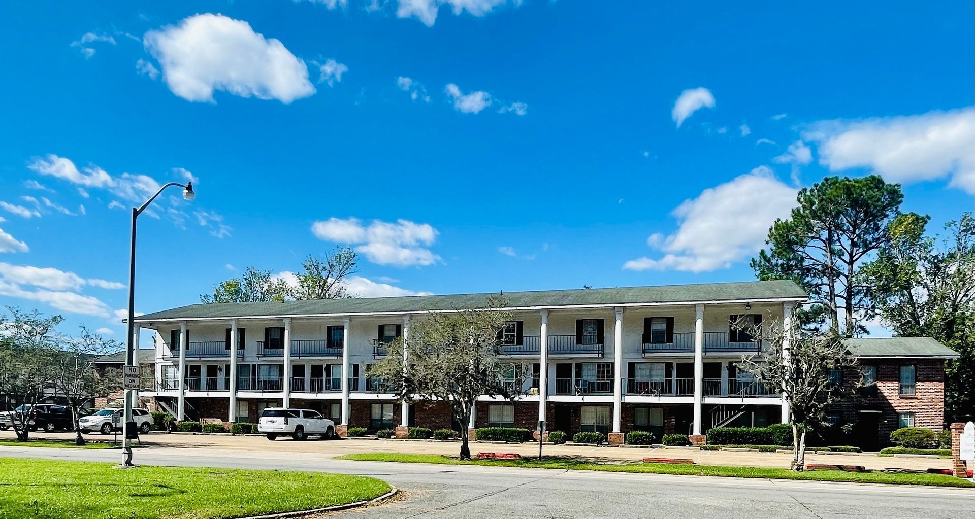Apartment building with white facade and balconies under a blue sky with clouds.