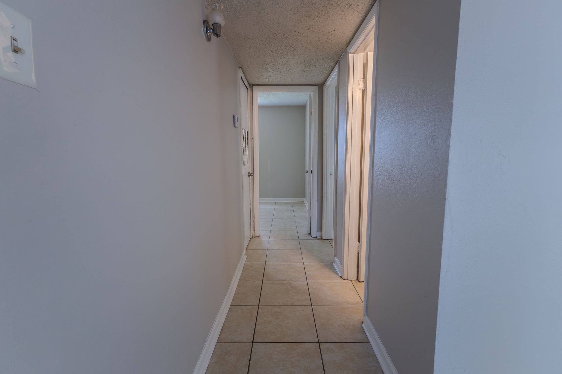 Narrow hallway with tiled floor, gray walls, and several doorways leading to other rooms.