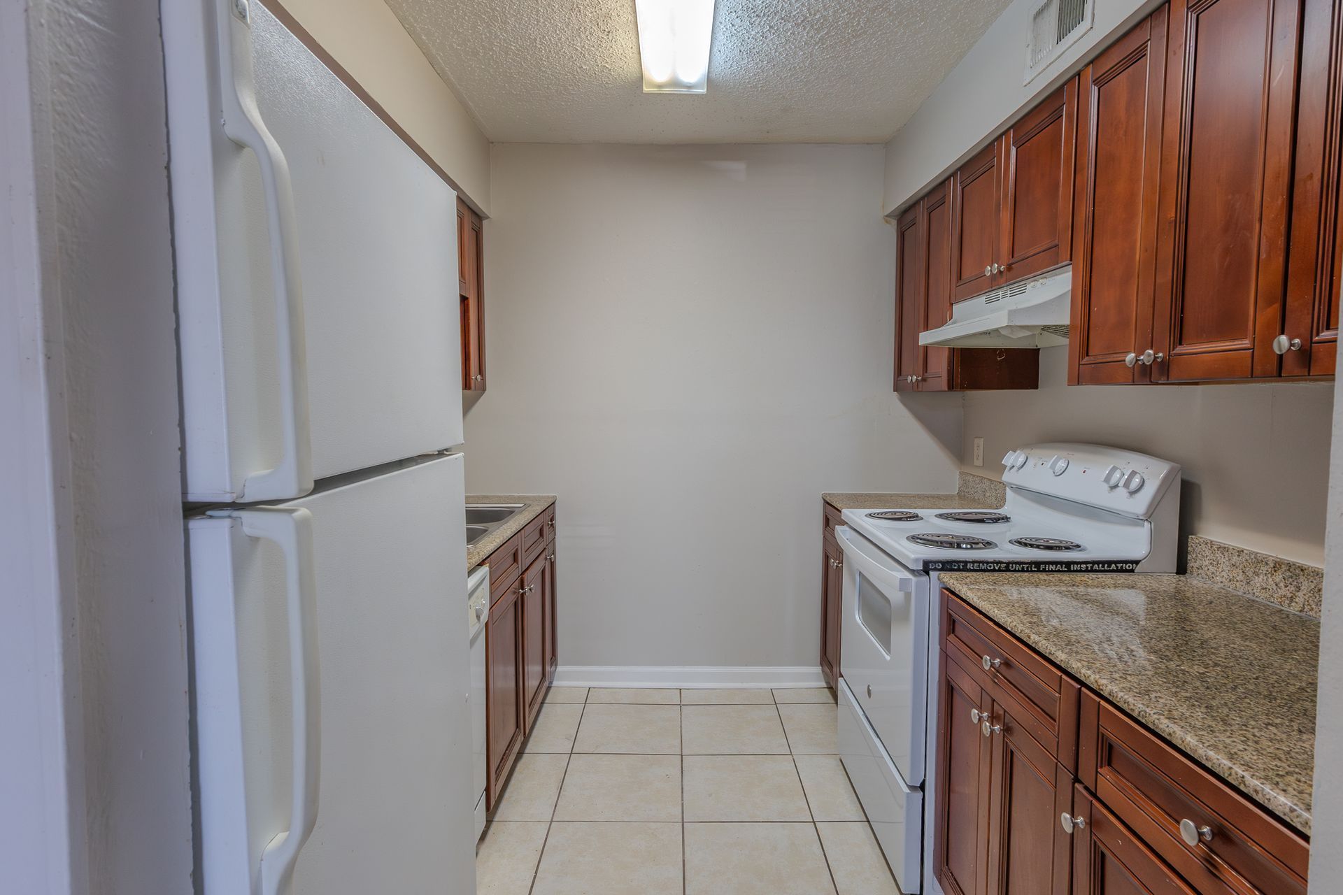 Narrow kitchen with white appliances, brown cabinets, and light countertops.