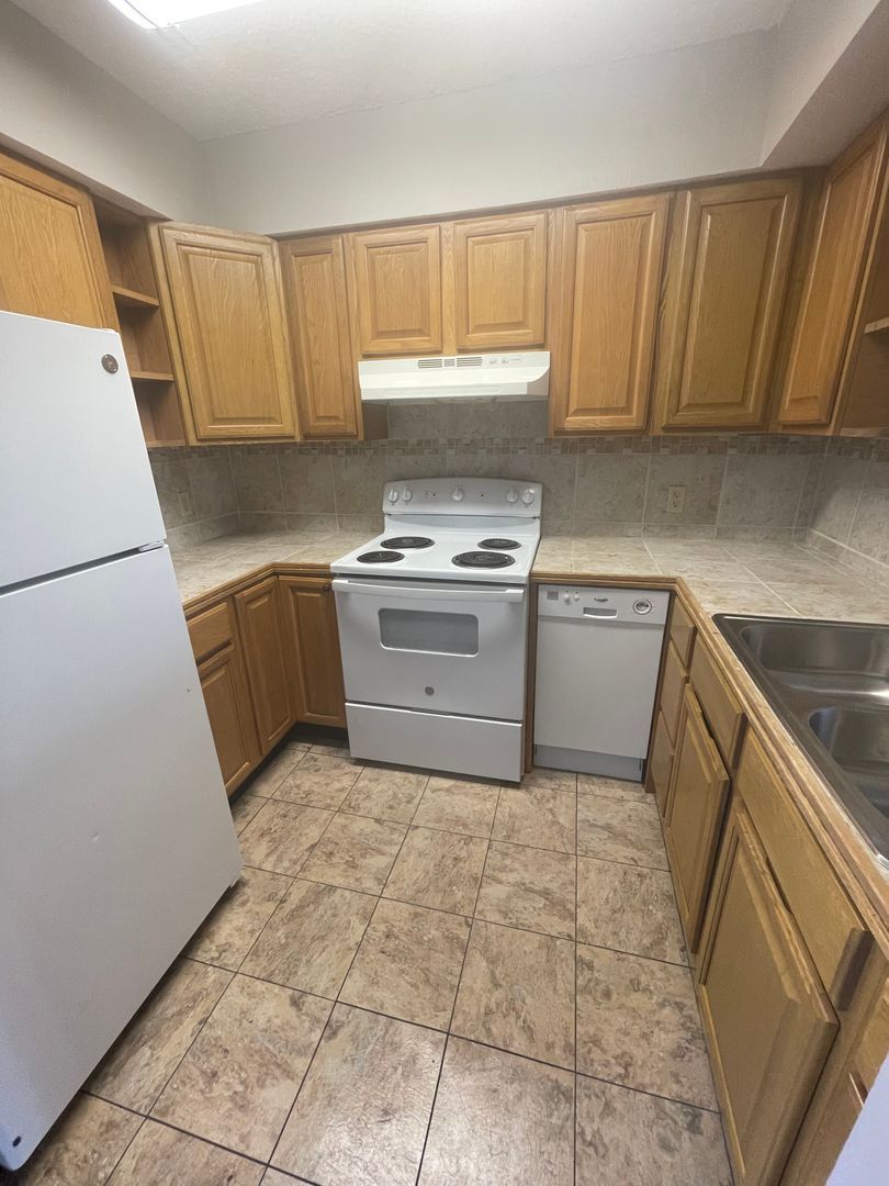 Kitchen with light wood cabinets, white appliances, and tiled floor.