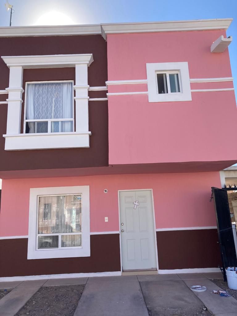 Casa de dos pisos con exterior rosa y marrón, marcos de ventanas blancos y puerta azul claro.