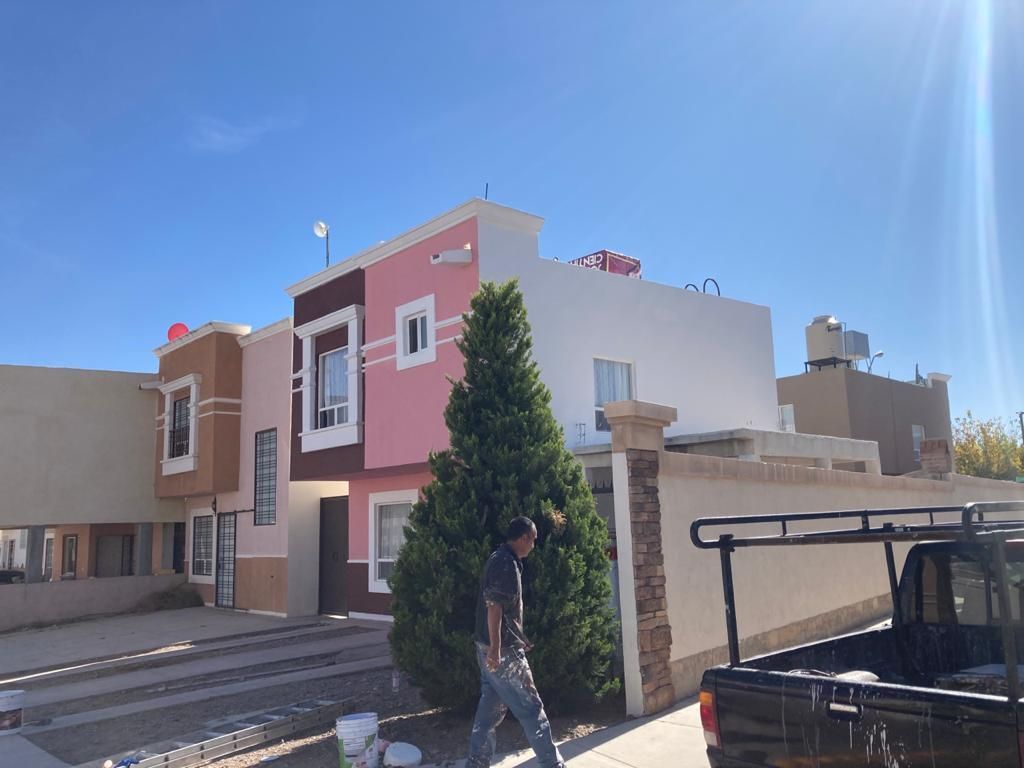 Una casa con paredes rosas y tostadas, un hombre al frente y un cielo azul.