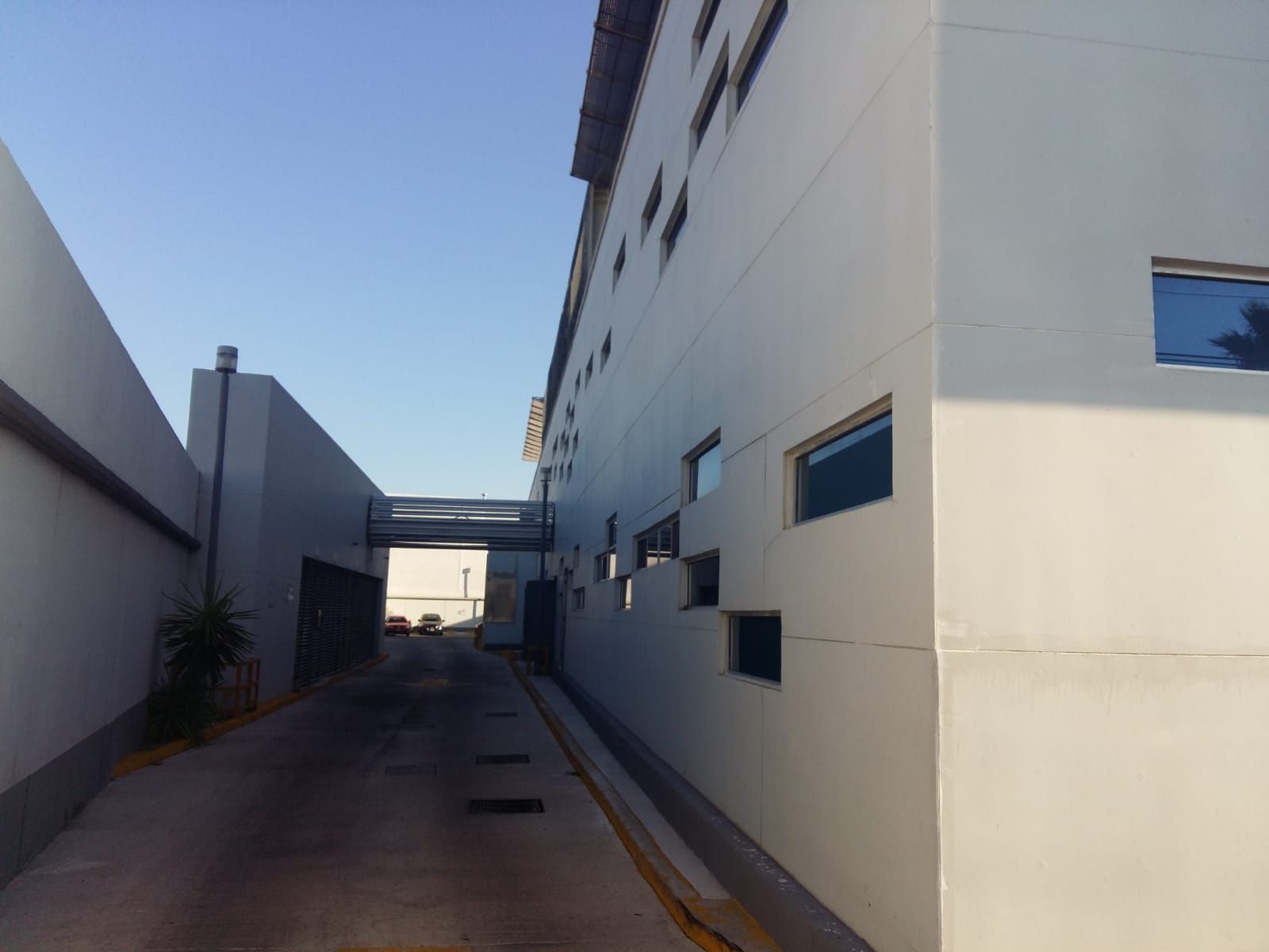Callejón entre dos edificios blancos; un puente peatonal los conecta. Cielo azul arriba.