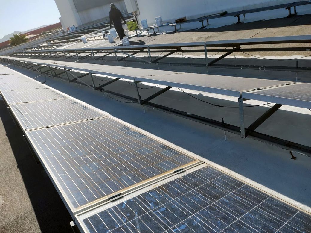 Paneles solares instalados en un techo comercial plano con una persona trabajando en el fondo.