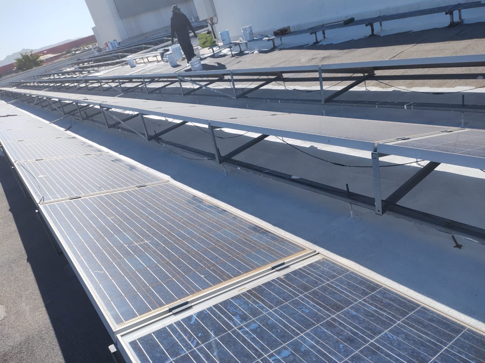 Paneles solares instalados en un tejado plano, con un trabajador al fondo. Día soleado.