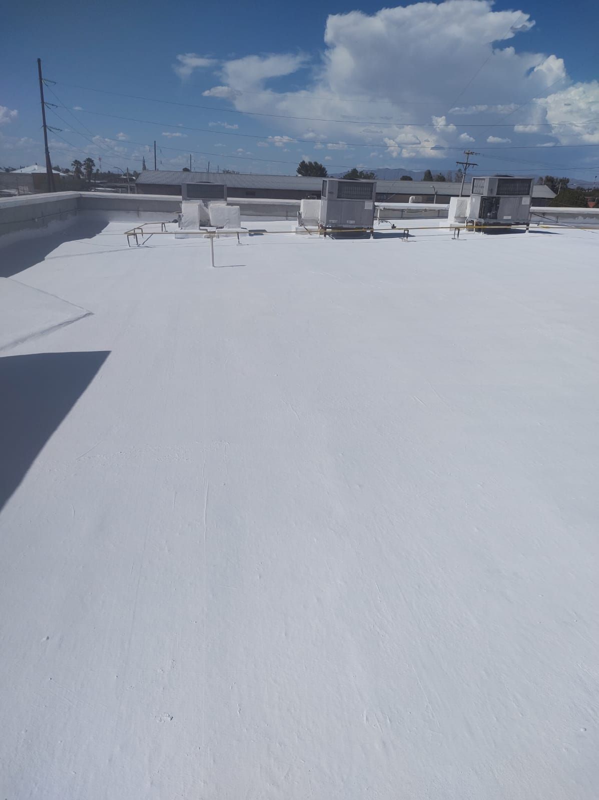 Techo comercial blanco con unidades de aire acondicionado contra un cielo azul con nubes.