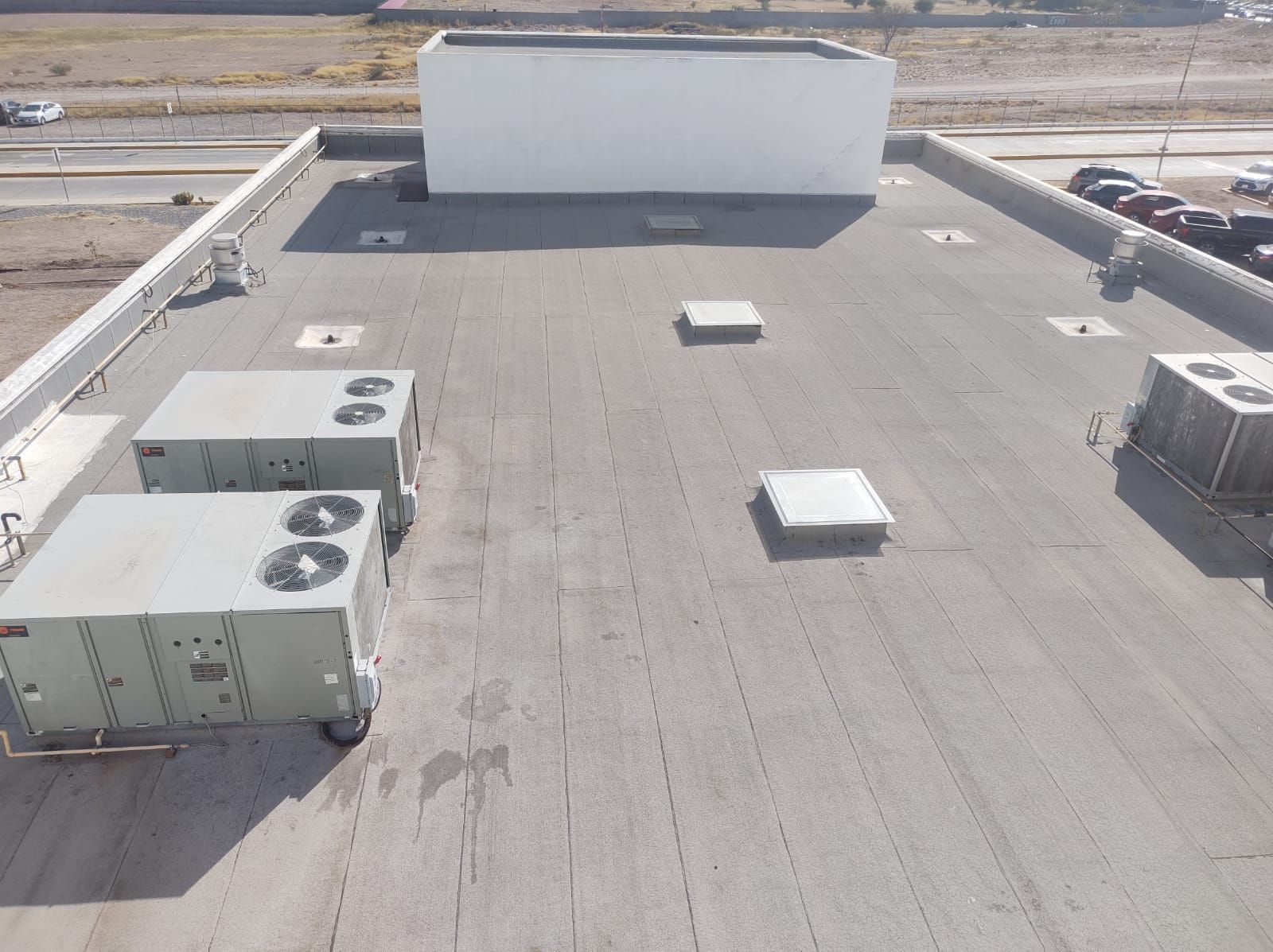 Una azotea comercial plana con unidades HVAC, ventilaciones y una estructura rectangular blanca.