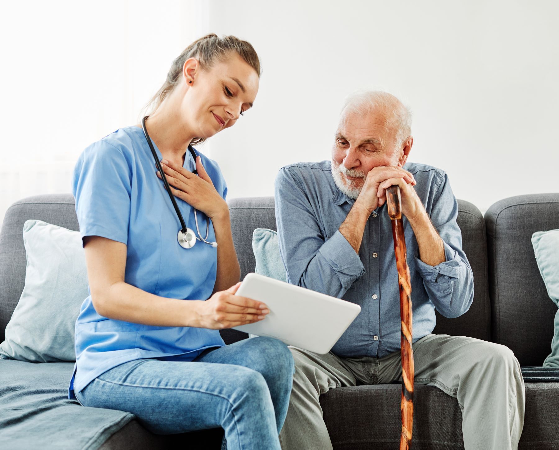caregiver showing tablet to senior patient on her left while both sit on couch