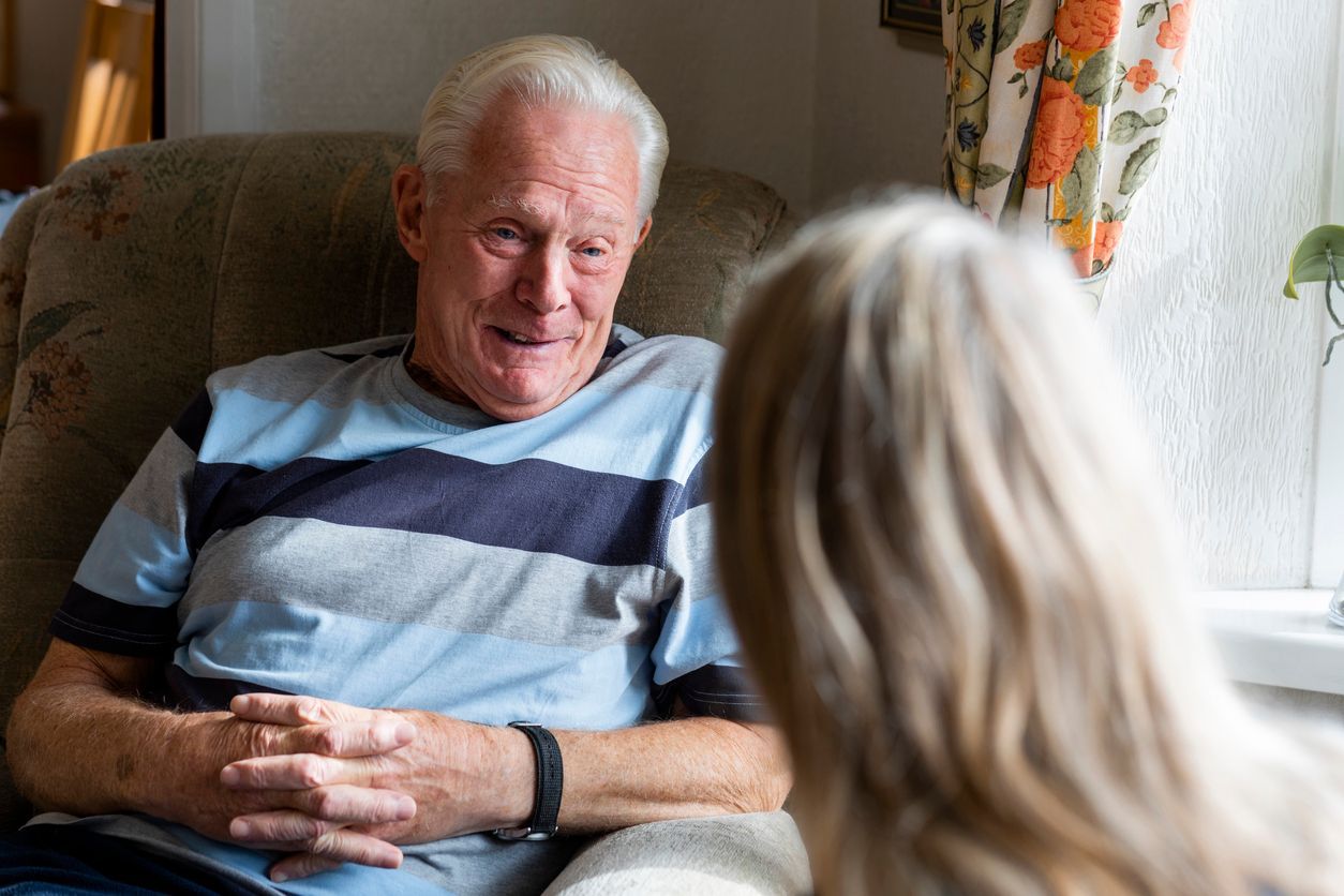 A woman conversing with a senior patient with dementia. The senior man is happy as he talks to the woman.