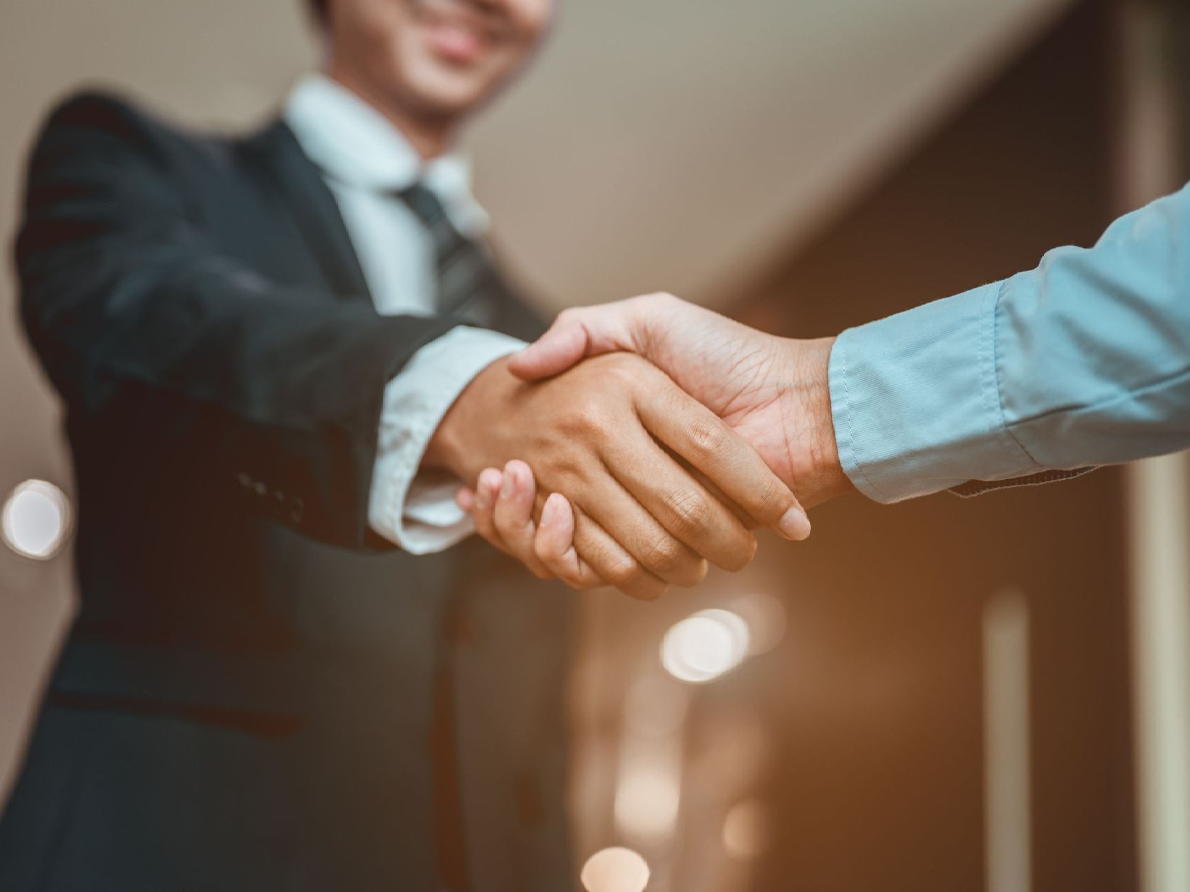 A man in a suit and tie is shaking hands with another man in a blue shirt.