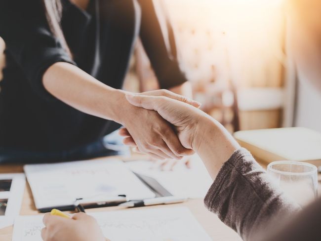 A man and a woman are shaking hands over a table.