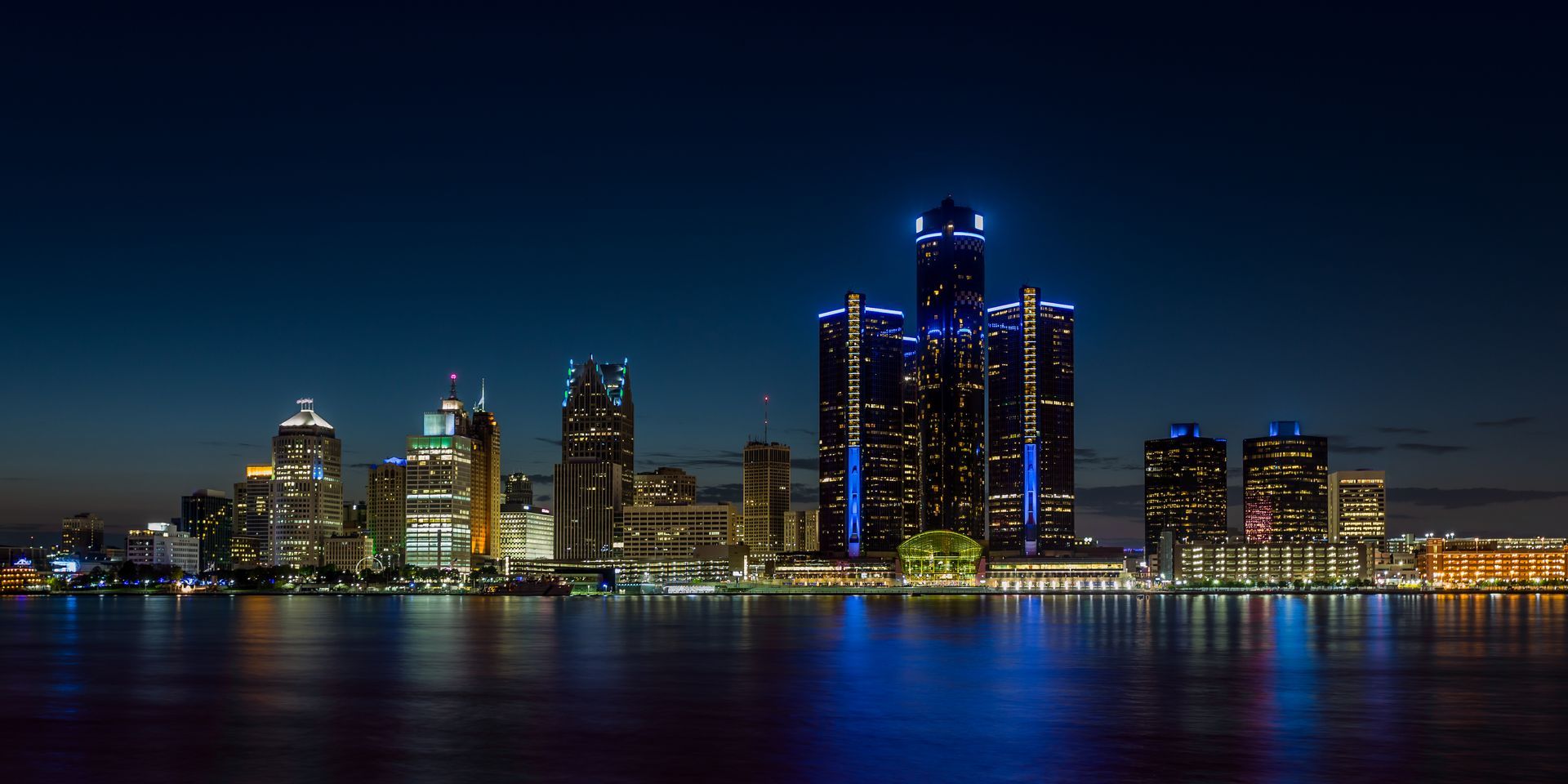 The city skyline is lit up at night and reflected in the water.
