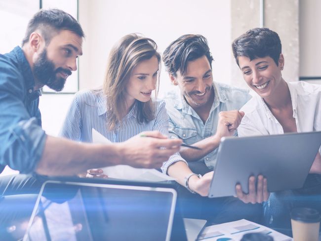 A group of people are sitting around a table looking at a laptop.