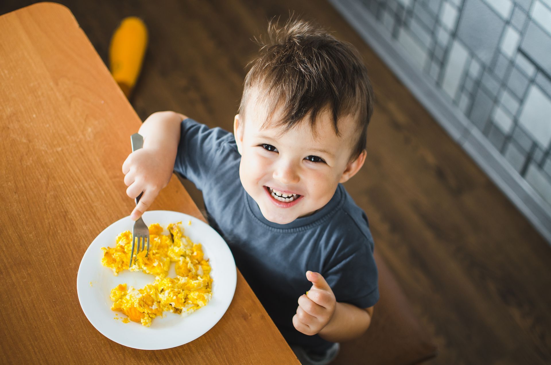 A little boy is sitting at a table eating scrambled eggs with a fork.