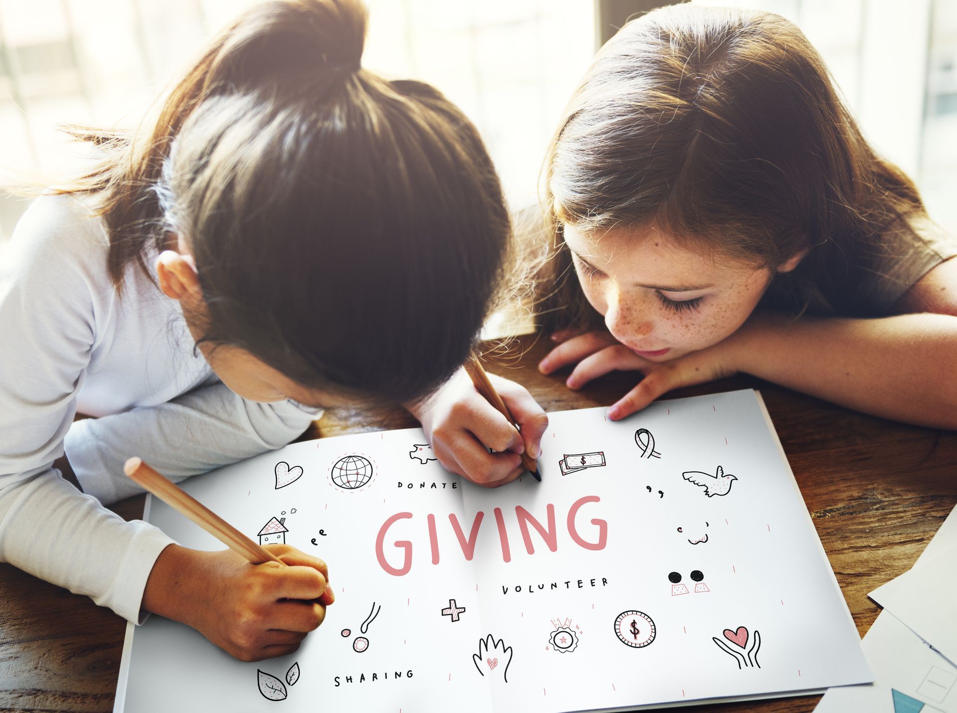 Two young girls are sitting at a table writing on a piece of paper.