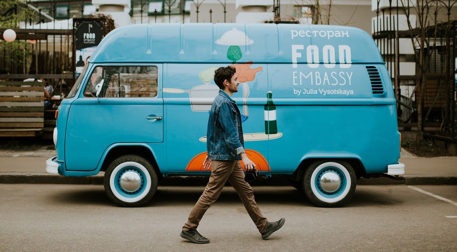 A man is walking past a blue food truck on the side of the road.