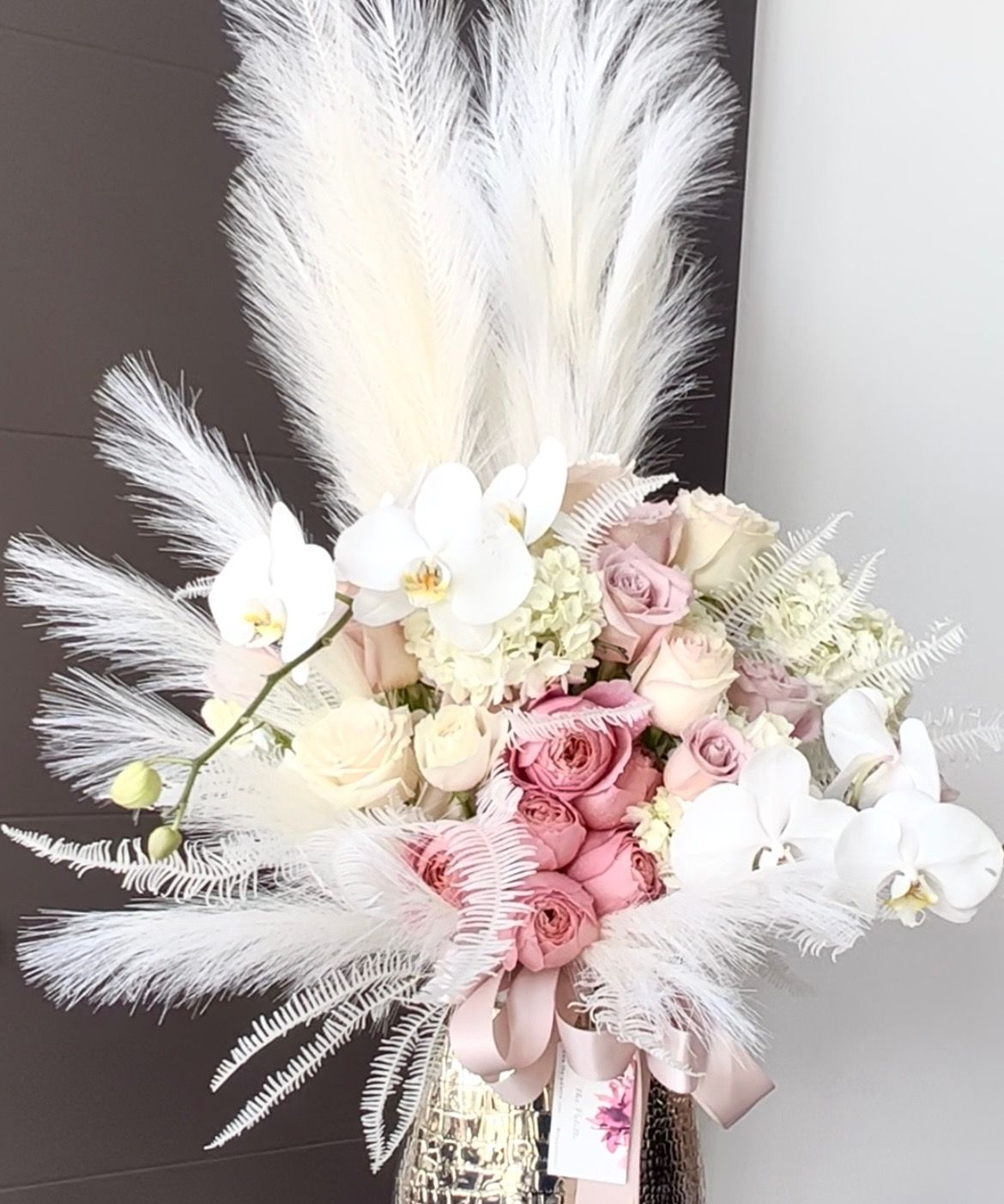 A vase filled with pink and white flowers and white feathers.