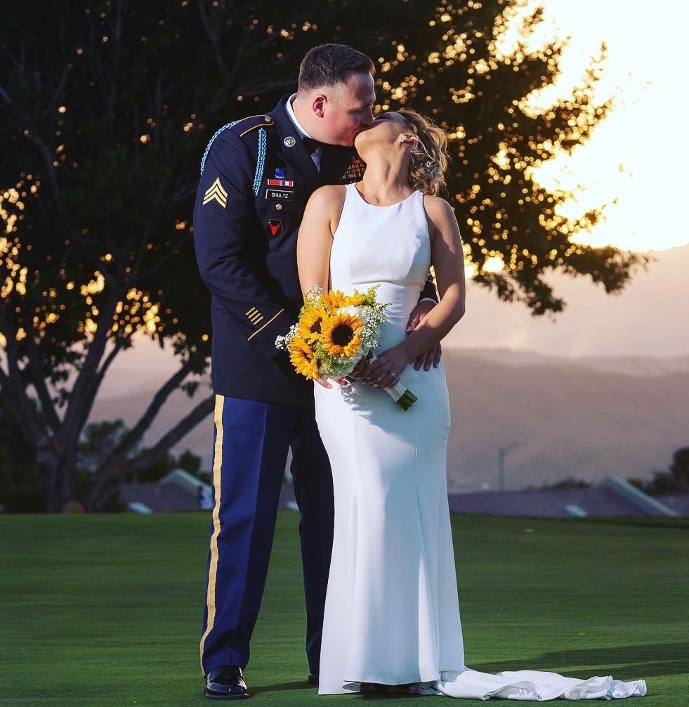 A man in a military uniform kisses a woman in a white dress