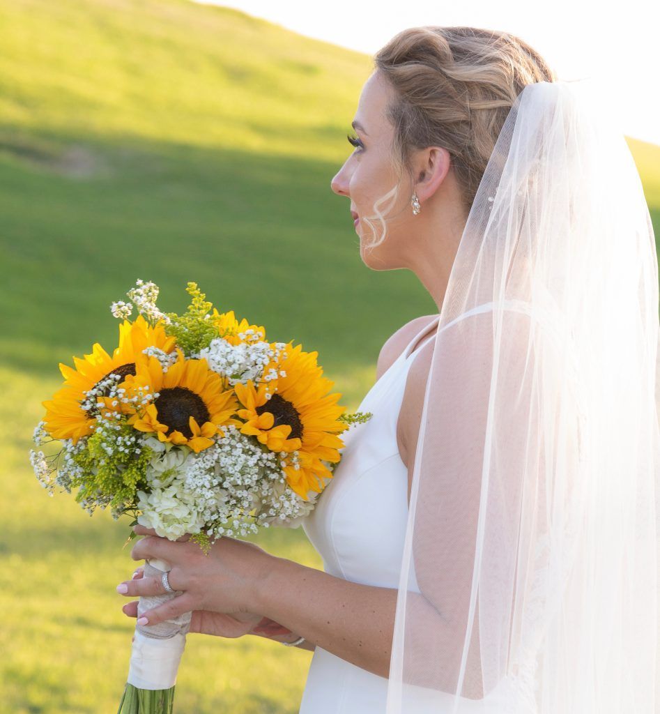 The bride is wearing a veil and holding a bouquet of sunflowers