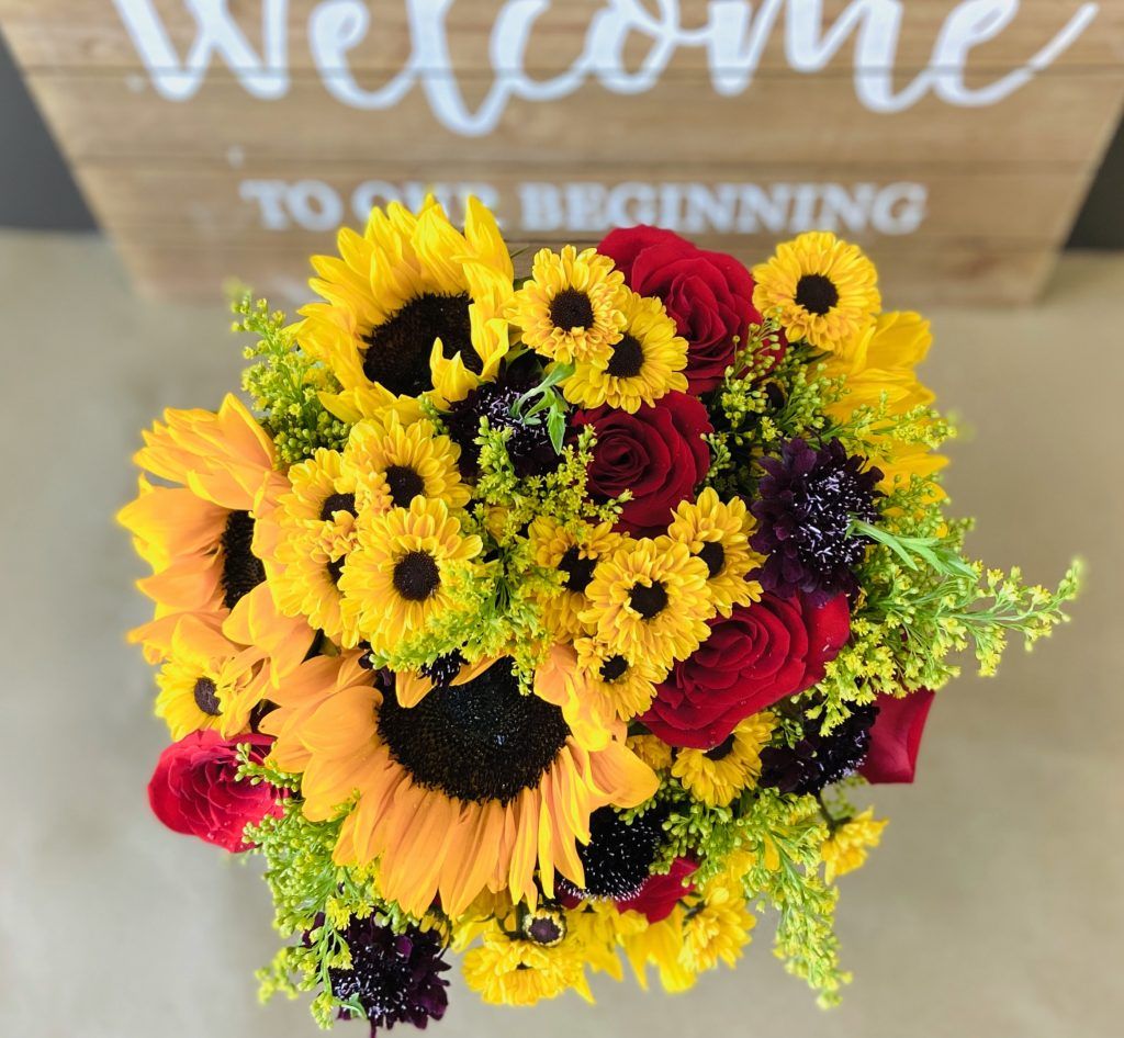 A bouquet of sunflowers and red roses in front of a welcome sign