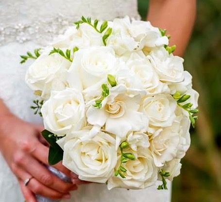 A bride in a white dress is holding a bouquet of white roses.
