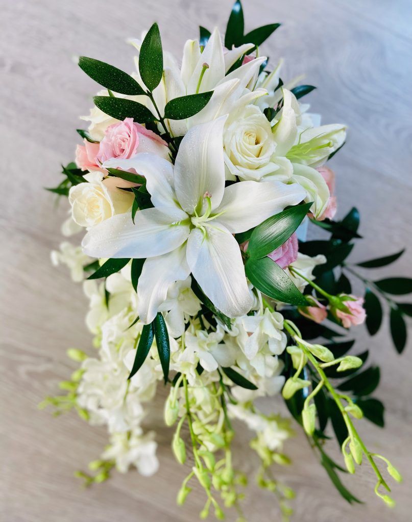 A bouquet of white flowers and pink roses is sitting on a wooden table.