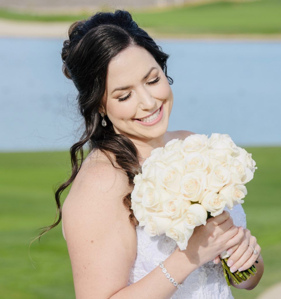 The bride is smiling while holding a bouquet of white roses.